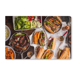 Obraz na płótnie Grill - kiełbasa, kanapki ze smażonymi ziemniakami i sosem podawanymi na rustykalnym stole